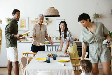 Smiling family setting table in kitchen - EBSF03679