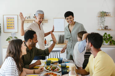Smiling family giving high-five on dining table in kitchen - EBSF03688