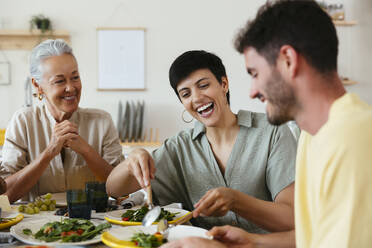 Lächelnde Mutter beim Mittagessen mit der Familie am Esstisch zu Hause - EBSF03697