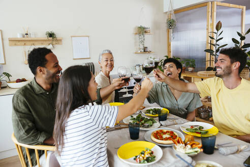 Cheerful family raising toast at dining table in kitchen - EBSF03699