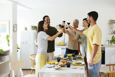 Happy family raising toast standing near dining table in kitchen - EBSF03700