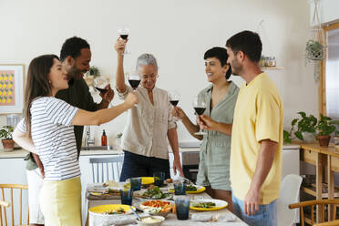 Smiling family raising toast standing near dining table in kitchen - EBSF03701