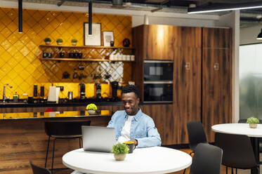 Smiling businessman working on laptop sitting at office - PGF01506