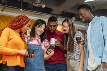 Geschäftsfrau teilt Smartphone mit Kollegen beim Kaffee im Büro - PGF01516