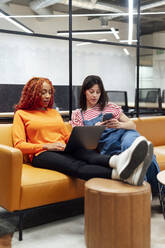 Businesswomen using wireless technologies sitting at office - PGF01553