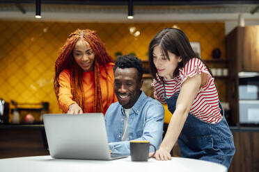 Lächelnde multiethnische Geschäftskollegen mit Laptop an einem modernen Arbeitsplatz - PGF01569