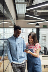 Smiling businessman with colleague using smart phone in office - PGF01604