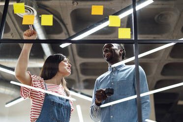 Happy businessman and businesswoman having discussion over adhesive notes - PGF01609