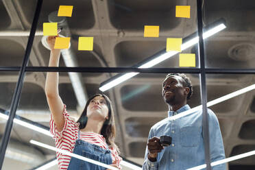 Smiling businessman and businesswoman having discussion over adhesive notes in office - PGF01610