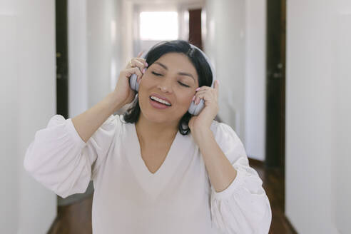 Smiling woman with headphones enjoying music at home - DSIF00679