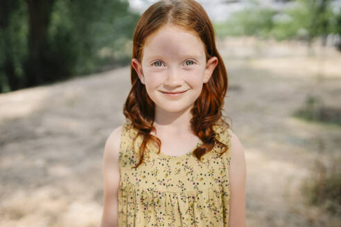 Smiling redhead girl standing in park - SSYF00175