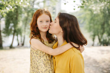 Loving mother kissing daughter in park - SSYF00178