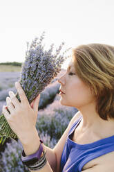Frau mit geschlossenen Augen riecht an einem Strauß Lavendelblüten im Feld - SIF00737