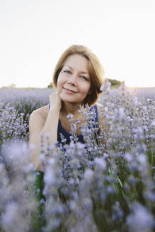 Lächelnde Frau hockt inmitten von Lavendelpflanzen im Feld - SIF00748