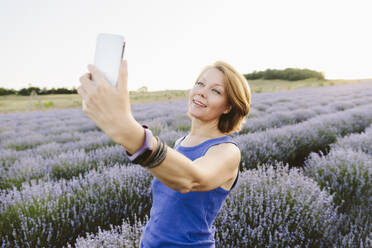Eine fröhliche Frau fängt einen Moment des Glücks ein, während sie für ein Selfie inmitten eines wunderschönen Lavendelfeldes posiert - SIF00751
