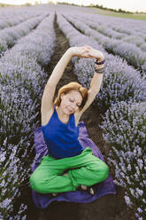 Lächelnde Frau bei einer Yogaübung inmitten eines Lavendelfeldes - SIF00758