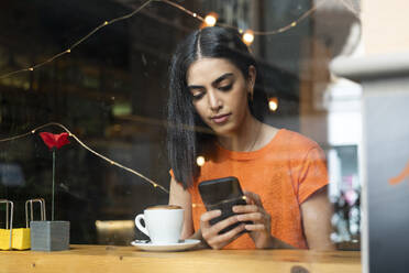 Junge Frau mit Smartphone in einem Café sitzend - LMCF00458