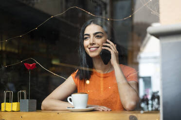 Lächelnde junge Frau, die in einem Café sitzt und mit ihrem Smartphone spricht - LMCF00459
