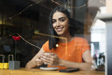 Lächelnde junge Frau, die in einem Café sitzend einen Kaffee genießt - LMCF00460