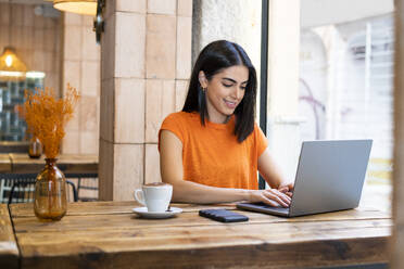 Young freelancer working on laptop sitting in cafe - LMCF00465