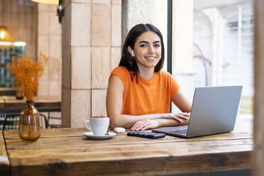 Smiling freelancer with laptop sitting at cafe - LMCF00468