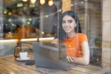 Smiling freelancer sitting with laptop at cafe - LMCF00474