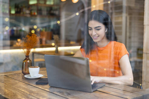 Lächelnder junger Freiberufler, der in einem Café am Laptop arbeitet - LMCF00475