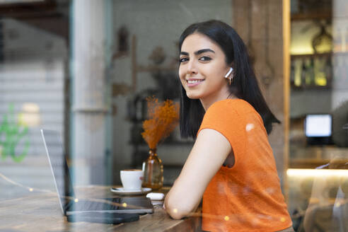 Smiling young businesswoman with laptop sitting in cafe - LMCF00478