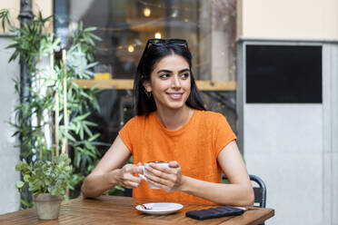 Thoughtful young woman enjoying coffee sitting at table in cafe - LMCF00479