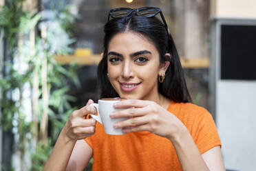 Lächelnde junge Frau genießt einen Kaffee im Café - LMCF00480