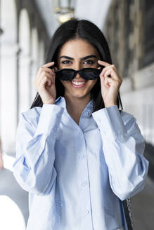 Lächelnde junge Frau mit Sonnenbrille auf einer Kolonnade - LMCF00487