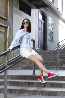 Happy young woman sitting on railing - LMCF00496