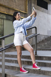 Eine junge Frau fängt einen Moment der Selbstdarstellung und des Selbstvertrauens ein, während sie ein Selfie auf einer Treppe macht - LMCF00497