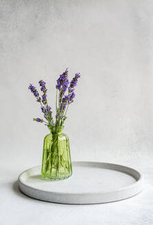 Minimalistic interior decor with lavender flowers in green glass vase on white table against white background - ADSF45888