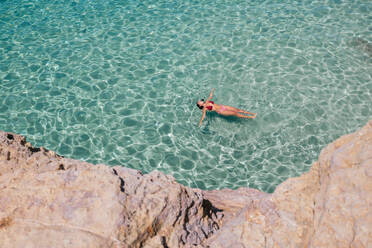 High angle of young female tourist in bikini floating in turquoise sea on summer vacation on tropical resort on Balearic Islands - ADSF45957