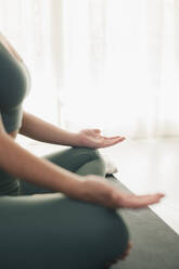 Side view of crop anonymous fit female in sportswear sitting on mat in lotus position and meditating while practicing yoga at home - ADSF45970