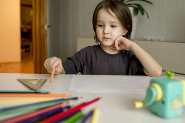 Thoughtful boy with colored pencils on table at home - ANAF01848