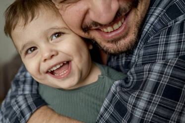 Smiling father embracing son at home - ANAF01857