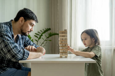 Sohn spielt Jenga mit Vater auf Tisch zu Hause - ANAF01860