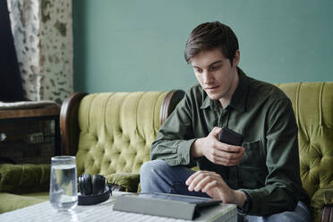 Junger Geschäftsmann sitzt am Tisch in einem modernen Café und benutzt einen Tablet-PC - DSHF00904