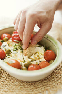 Hand einer Person, die gebackenen Feta-Käse mit Oliven, Kirschtomaten und Kräutern isst - ONAF00611