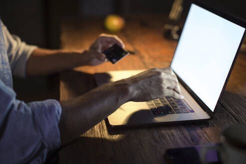 Freiberufler, der eine Kreditkarte zur Bezahlung auf einem Laptop im Home Office verwendet - IKF01006