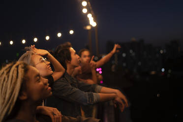 Lächelnde Freunde stehen nachts auf dem Dach - IKF01020