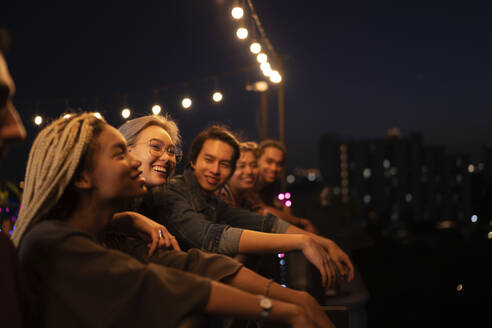 Smiling friends spending leisure time on rooftop at night - IKF01025
