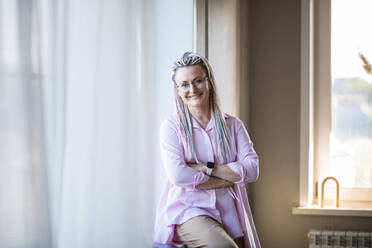 Smiling woman sitting with arms crossed at home - ADF00126