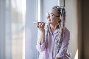 Smiling swoman recording voicemail on smart phone at home - ADF00127