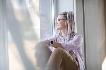 Contemplative woman sitting near window at home - ADF00130