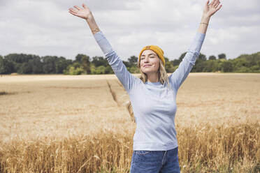Smiling woman with arms raised and eyes closed standing at field - UUF29658