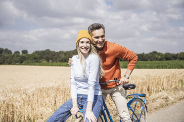 Glückliche Frau auf einem Fahrrad sitzend mit einem Mann auf einem Feld - UUF29659