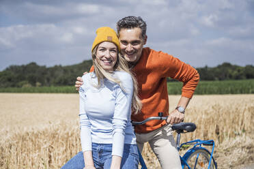 Glücklicher Mann und Frau mit Fahrrad auf einem Feld - UUF29663